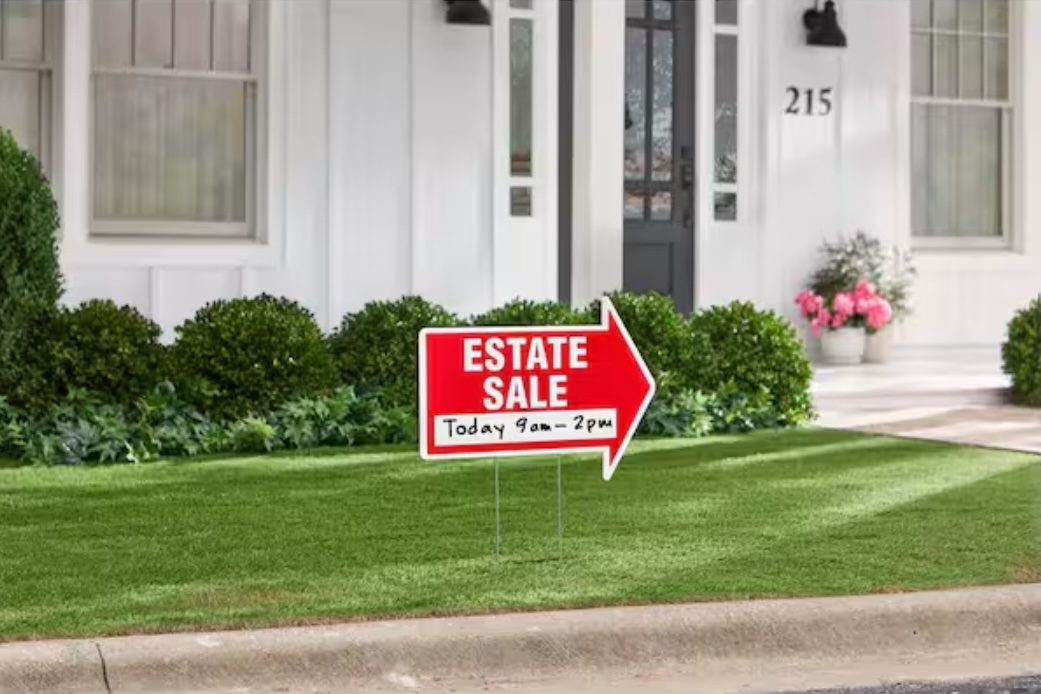 A red Estate Sale yard sign with arrow, posted on the lawn in front of a house