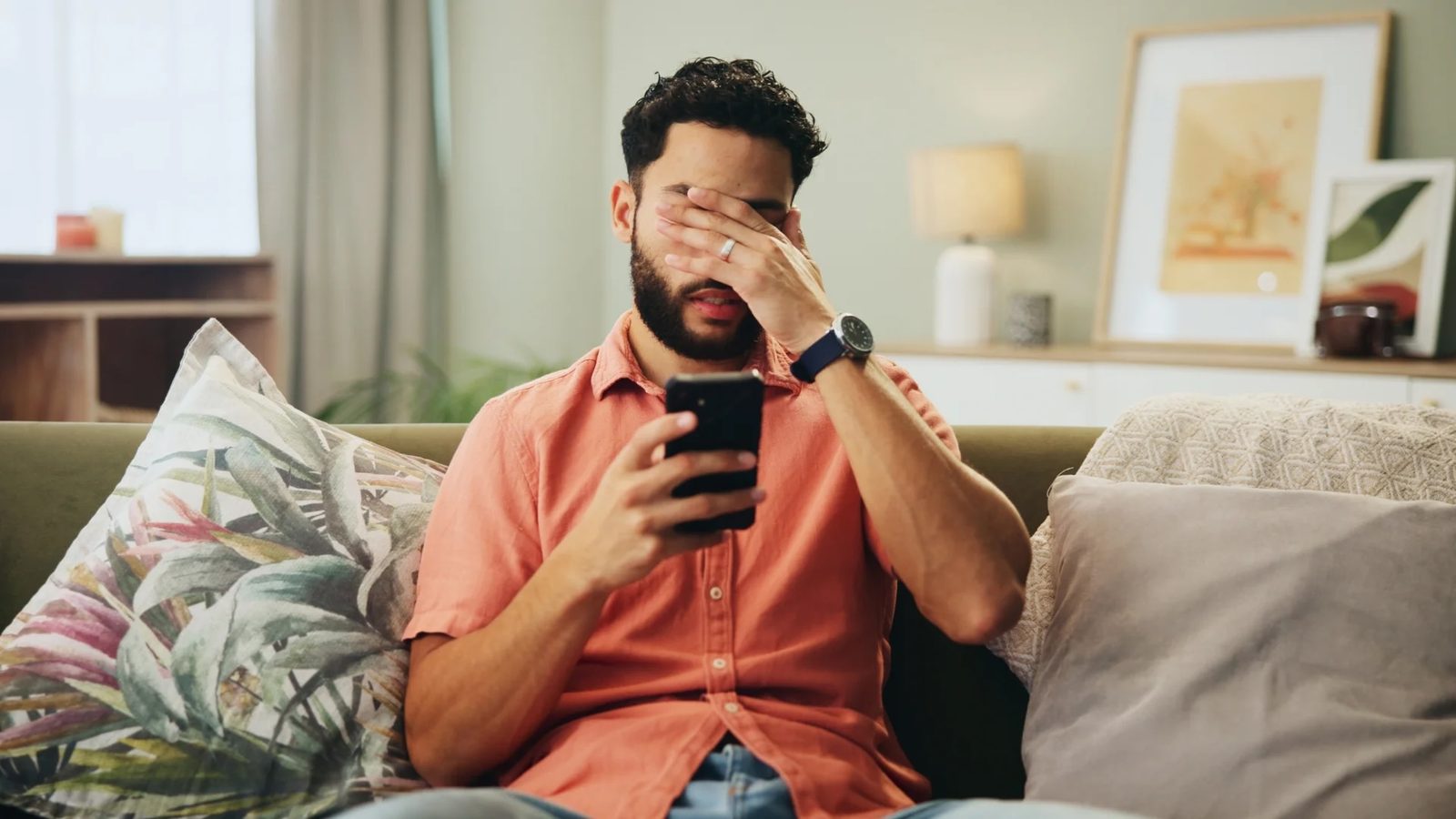 A man looking stressed while reading his phone on a couch