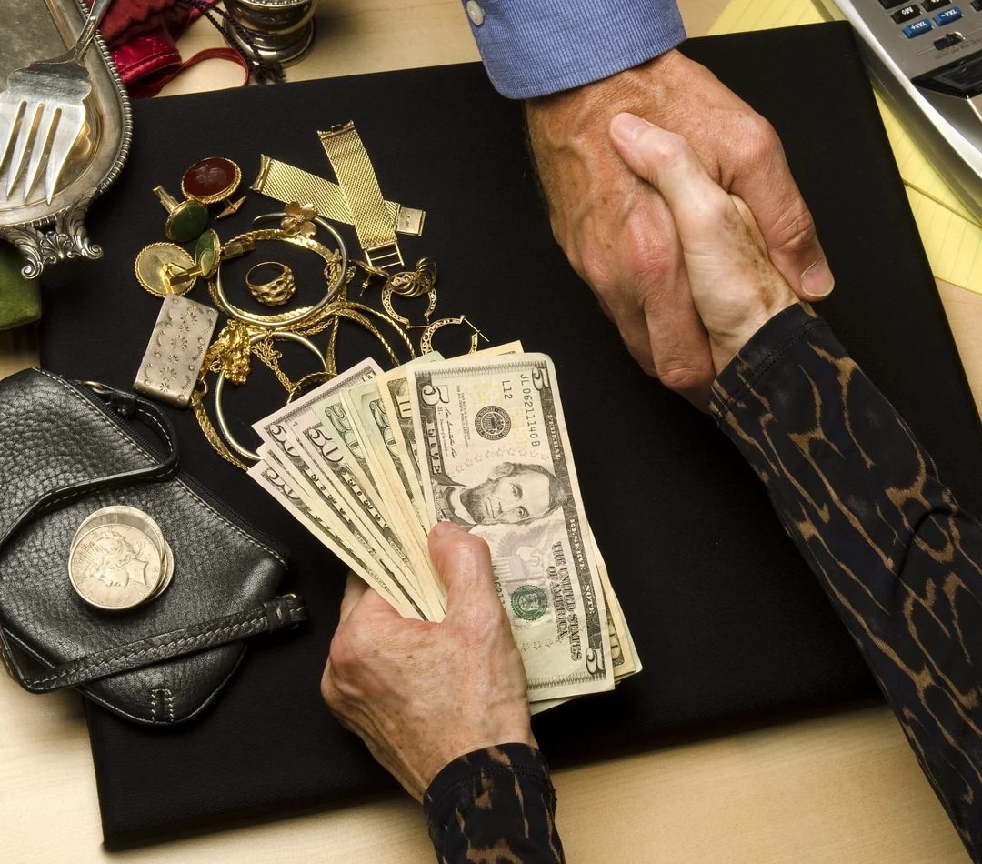Hands exchanging cash for jewelry, silver, and coins on a table